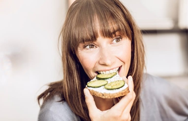 A person eating a piece of bread with cucumbers for best foods to boost ovulation