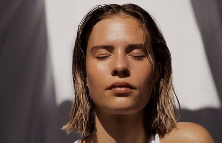 woman enjoying the warmth of sunlight on her clean face, eyes closed for herbs for acne