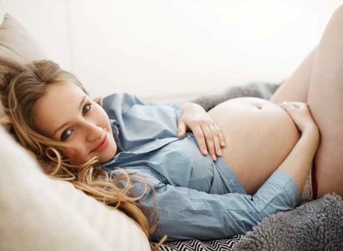 A pregnant woman lying on a couch cradling her baby belly for weight and fertility