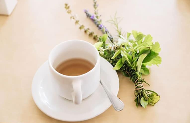 cup of herbal tea on table with bundle of fresh herbs for teas for healthy skin blog