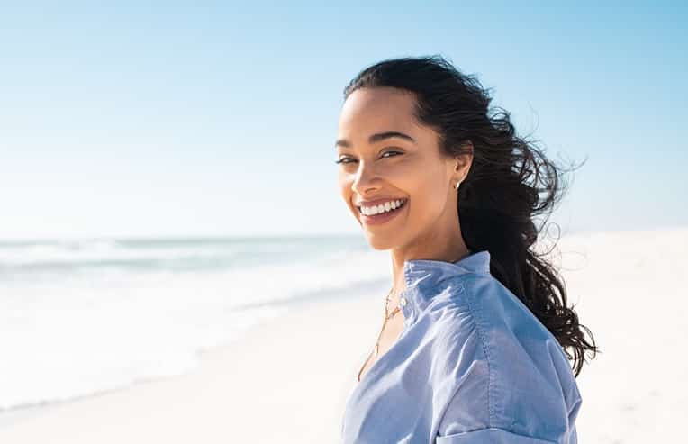 A woman smiling at the camera standing on the beach with wind in her hair for symptoms of perimenopause