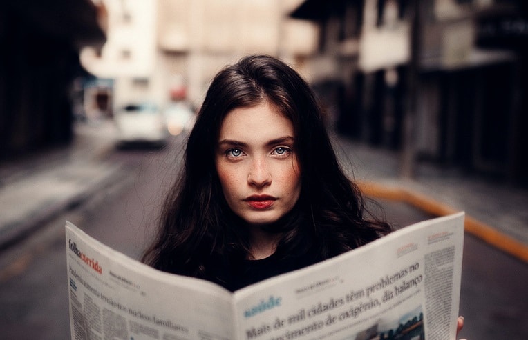 A woman looking forward over a newspaper for how toxins affect hormones and fertility
