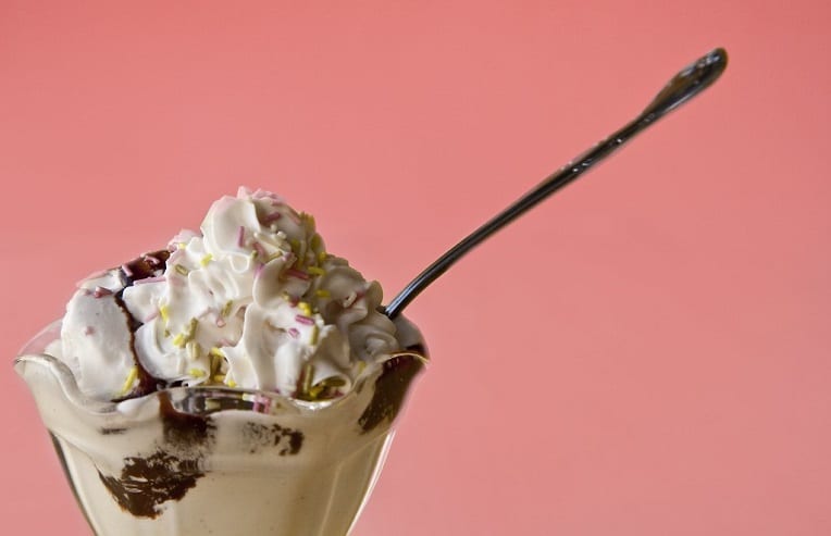 ice cream sundae with a spoon on salmon pink background for food cravings meaning