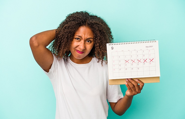 young african american woman holding a calendar marking her mentrual cycle looking uncomfortable